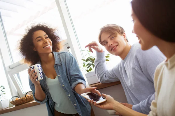 Ein bild von afroamerikanerin firl i, wie sie ihrem freund ein telefon gibt und lächelt. es gibt auch einen Kerl, der mit ihnen sitzt und asiatische Mädchen ansieht. — Stockfoto