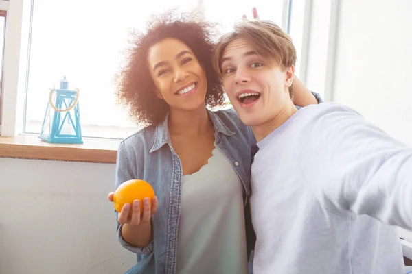 Två glada studenter tar selfie. Flickan håller en orange ana leende medan killen håller en kamera och laking bilder. — Stockfoto