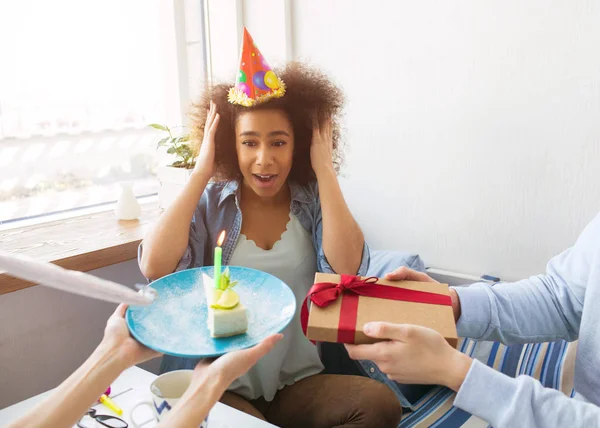 Сьогодні день народження дівчини у блакитній сорочці. Її друзі зробили їй несподіванку. Вони тримають подарунок і шматочок торта зі свічкою на ньому. Гільєрка на день народження тримає капелюх руками . — стокове фото