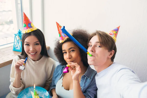 Guy se está tomando una selfie con sus dos amigos. Están celebrando el cumpleaños de las chicas afroamericanas. La gente usa sombreros de cumpleaños. También las niñas tienen whisltes . — Foto de Stock