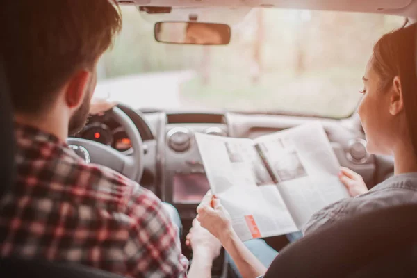 Una pareja joven está viajando. Viajan en coche. La chica tiene un mapa y míralo mientras conduce. Están siguiendo el camino . — Foto de Stock