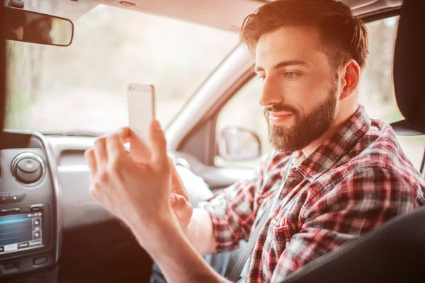 Un type sympa prend une photo de son partenaire au téléphone blanc. Il regarde l'écran et sourit un peu. Guy a l'air bien et confiant . — Photo