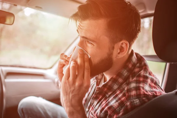 A picture of sick guy sneezing in napkin. He is looking straight. Young man is suffering.