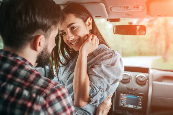 Una pareja encantadora está sentada sola en el coche. La chica está sentada cara a cara con su novio. Ella mantiene su mano cerca de la chica. Esta señora está sonriendo. Parece feliz. . — Foto de Stock