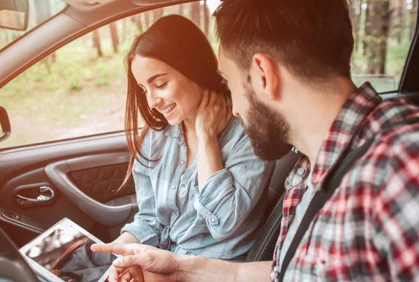 Belle fille est assise avec son petit ami en voiture et regardant l'écran. Elle se tient la main sur le cou les yeux fermés et souriant. Elle a l'air heureuse. Le gars pointe du doigt à l'écran . — Photo