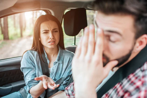 Beautiful girl is arguing with her boyfriend. She is not satisfied. Guy is covering his face with hand. He is very tired of that. They are sitting in car. — Stock Photo, Image