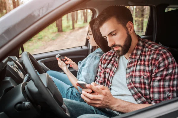 Два занятых человека сидят в машине и смотрят на свои телефоны. Они не разговаривают друг с другом. Они остановились в лесу. . — стоковое фото