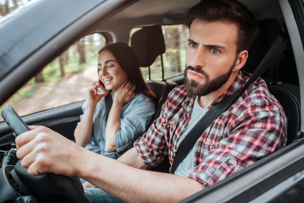 Jeunes femmes est assis à côté de l'homme qui conduit une voiture. Il est contrarié et malheureux. Le gars regarde du côté avec un visage sérieux — Photo