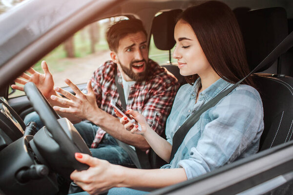 Angry and upset man is screaming and yelling at his girlfriend. He is very emotional. Girl is looking at the phone. She is not paying attention to the road.