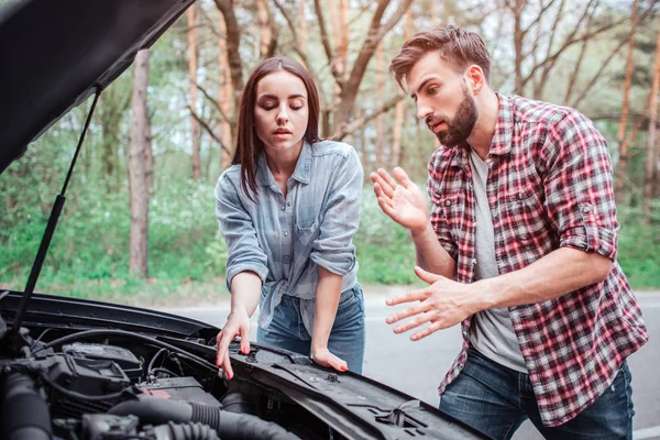 Una foto de una pareja tratando de arreglar el motor del coche. Se rompió. Chica está apuntando a motor mientras chico está hablando con ella y conseguir sus manos limpias . — Foto de Stock