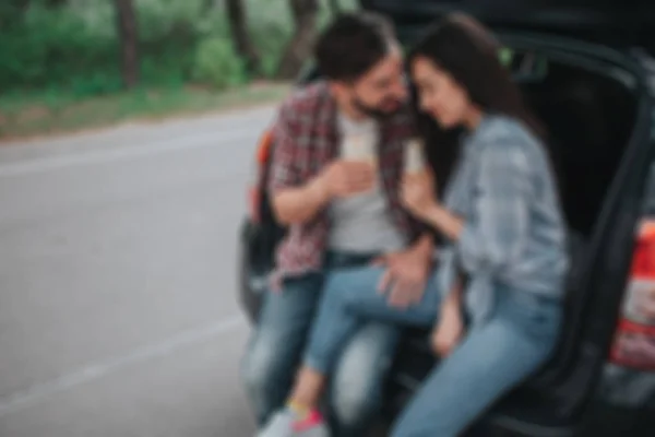 Размытое изображение молодой пары, сидящей в багажнике и держащей рулоны в руках. Парень смотрит на девушку. Она прислонилась к его плечу. Они выглядят счастливыми. . — стоковое фото