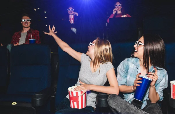 Funny picture of girls sitting together in cinema hall. They are looking at the boy that sits behind them. Blonde girl is trying to reach guy with her hand. Young woman are laughing. — Stock Photo, Image
