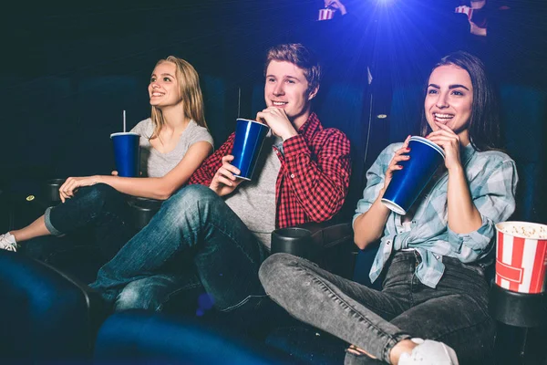 Nice people are sitting together in a cinema room. They are drinking coke and having fun. All of them are smiling and all of them has pun one leg on another. — Stock Photo, Image