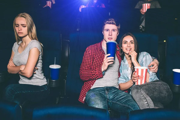 Beautiful couple is sitting together and watching movie. Brunette girl is eating popcorn and guy is drinking coke. She is offended of being alone. — Stock Photo, Image
