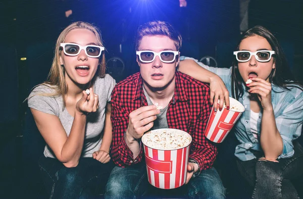 Beautiful people in glasses are looking straight forward. They has opened their mouthes. Each of them has a piece of popcorn in their hands. They look excited. — Stock Photo, Image