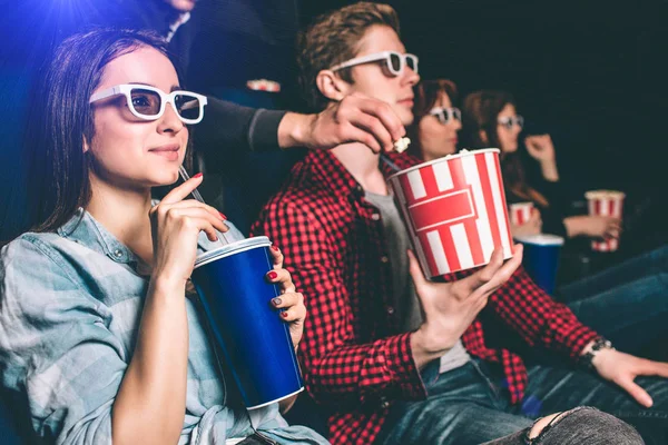 Somebody is reaching to the basket with popcorn that guy has and trying to take some popcorn from it. Guy doesnt see it because he is watching movie. Girl doesnt see it too. She holds a cup of coke. — Stock Photo, Image