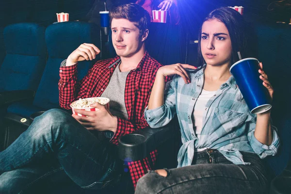 Stilig kille och vacker flicka sitter tillsammans och titta på film. Händerna rätt poserar. Flickan håller en kopp av koks medan killen har en korg med popcorn. — Stockfoto