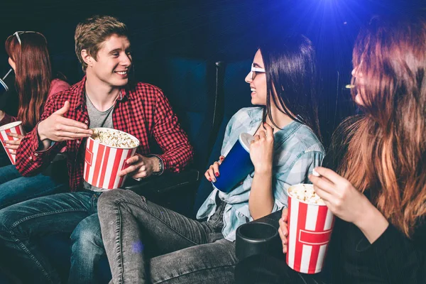 Nice guy is proposing his popcorn to a girl. Two girls are looking at him and smiling. Brunette girl is impressed. She is holding a cup of coke while her friend has a small basket of popcorn. — Stock Photo, Image