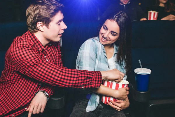 Hodný člověk dosahuje na popcorn. Jeho přítelkyně má busket to. Také ona má šálek koksu vedle ní. Ona se na něj dívá a usmívá se. — Stock fotografie