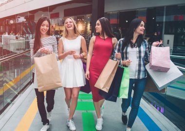 Güzel kızlar birlikte alışveriş merkezinde yürüyüş mesafesindedir. Onlar alışveriş vardır. Genç kadınların ellerinde çanta var. Kızlar gülen ve having fun.
