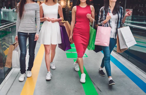 Vista cortada de las niñas caminando juntas en una gran tienda. Llevan ropa diferente y tienen diferentes bolsas de colores en sus manos. Las mujeres jóvenes están de compras . — Foto de Stock