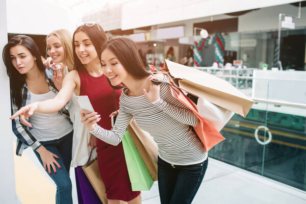 Cheerful and happy girls are standing one after another and looking down. Girl in red dress is pointing while asian girl is taking picture.