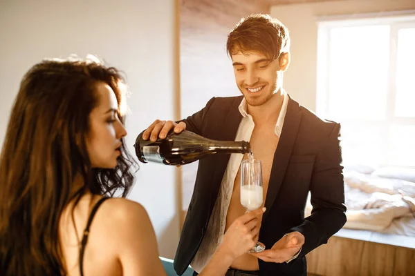 Unga sexiga par i vardagsrummet. Glada trevlig affärsman i kostym häller mousserande vin i kvinnors glas. Tillsammans i rummet. Sexig souple efter intimitet. — Stockfoto