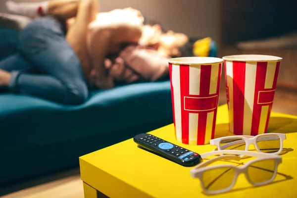 Young couple have intimacy in kitchen in night. Blurred background. Popcorn buckets with cinema glasses and remote control on table. Man on top. Hot sensual woman lying on sofa. — Stock Photo, Image