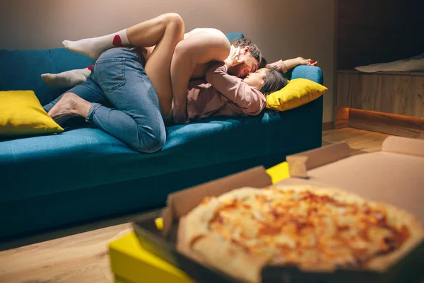 Genç çiftler geceleri mutfakta yakınlaşırlar. İyi yapılı üstsüz bir adam baştan çıkarıcı bir kadını öpüyor. O, onu bacaklarıyla kucakladı. Seks pozisyonu. Tutku ve şehvet. Pizza hazır.. — Stok fotoğraf