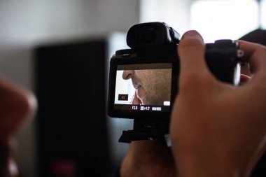 Görüntüyü kesin ve kameramanların kamerayı ayarlayan ellerini kapatın. Video kaydediyor ya da genç adamın yüzünün fotoğrafını çekiyor. Odadaki işlemin yan görüntüsü. Bulanık arkaplan.