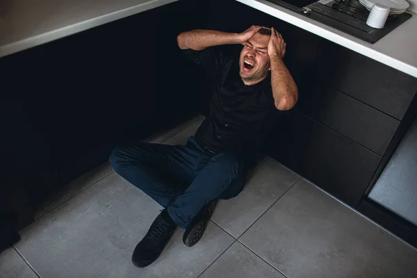 Imagem colorida de homem louco desparate sentado no chão na cozinha e gritar. Mãos na cabeça. Problemas psicológicos e desordem. Depressão e loucura . — Fotografia de Stock