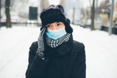 Genç bir kadın hastalık koronavirüs koruması için yüz maskesi takıyor. Kadın portresi baş ağrısı ya da ağrıdan dolayı el ele tutuşuyor. Enfeksiyon kapmış vücut. Hastalık ve hastalık.