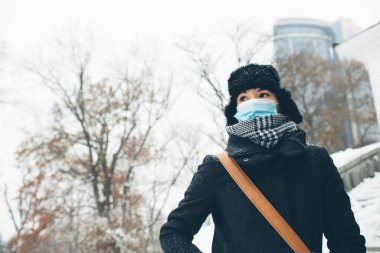 Genç bir kadın hastalık koronavirüs koruması için yüz maskesi takıyor. Dişi insan kışın dışarıda kalın giysiler giyer. Enfeksiyona hazır olun. Tehlike ya da hastalığa..