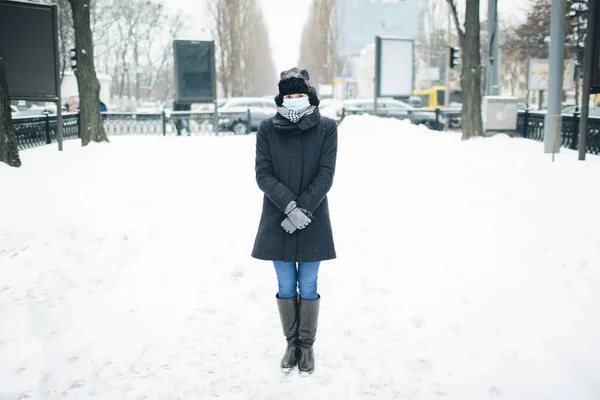 Mujer joven usar mascarilla para la protección contra el coronavirus enfermedad. Imagen de una joven hembra delgada parada en medio en terreno lento en invierno. Prepárate para la infección peligrosa o enfermedad . — Foto de Stock