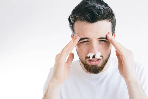 Baş ağrısı ve acı içinde alnını tutan genç hasta bir adamın portresi. Burun aksırması. Coronavirus. Esmer sakallı adam arka planda izole edilmiş.. — Stok fotoğraf