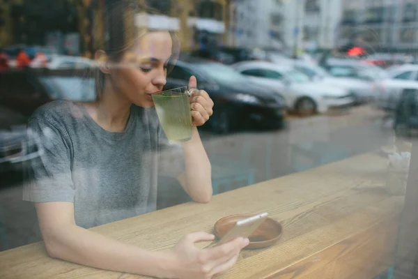 De blonde gebruikt de telefoon. Meisje en smartphone. Een vrouw zit in een café met een mobieltje. — Stockfoto