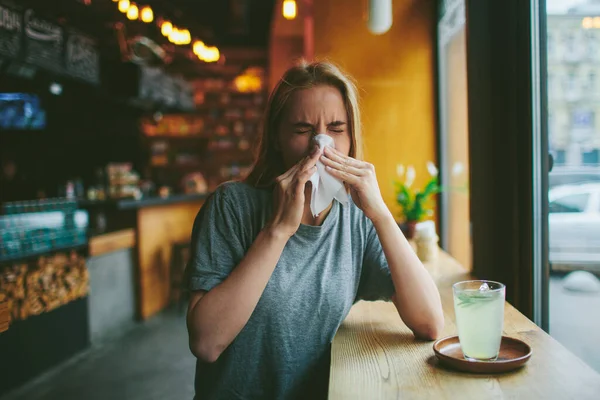La joven rubia en un café se sonó la nariz. Tiene secreción nasal. En la mesa hay una taza de té. . — Foto de Stock