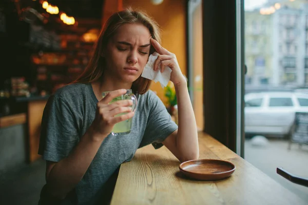 Jong blondje in een café. Ze heeft een verkoudheid en een loopneus, haar hoofd doet pijn. Ze heeft een kop hete thee. — Stockfoto