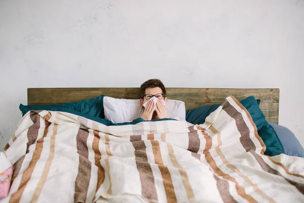 Anak muda dengan saputangan. Orang sakit di tempat tidur memiliki hidung berair. manusia membuat obat untuk flu biasa — Stok Foto