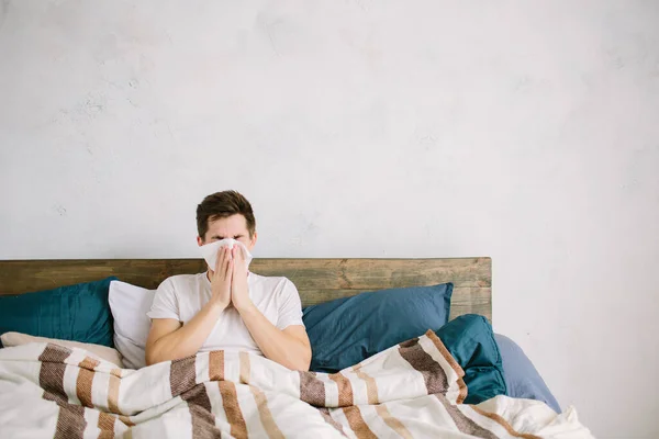 Anak muda dengan saputangan. Orang sakit di tempat tidur memiliki hidung berair. manusia membuat obat untuk flu biasa — Stok Foto