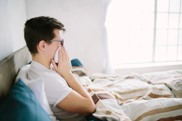 Junger Mann mit Taschentuch. Kranker Kerl auf dem Bett hat laufende Nase. Mann macht Heilmittel gegen Erkältung — Stockfoto