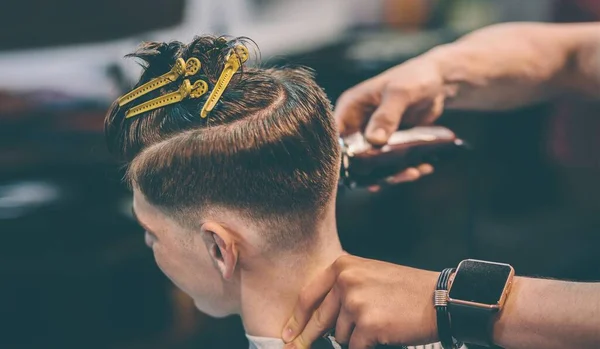 Cabeleireiro faz penteado um homem com um clipe na cabeça em um salão de cabeleireiro . — Fotografia de Stock