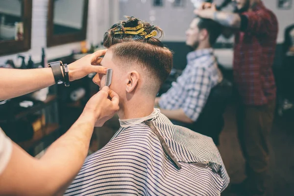 Cabeleireiro faz penteado um homem com um clipe na cabeça em um salão de cabeleireiro — Fotografia de Stock