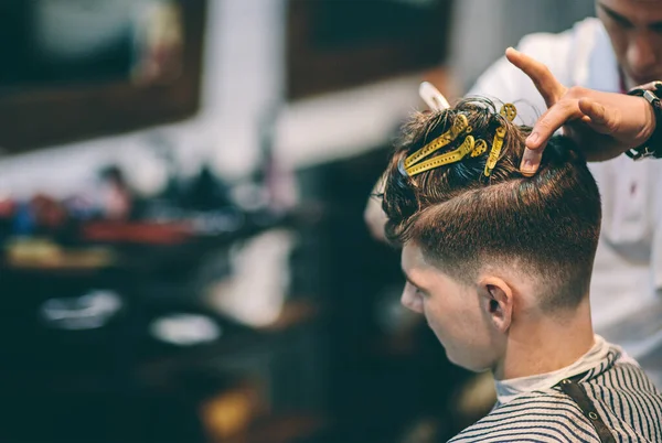 Cabeleireiro faz penteado um homem com um clipe na cabeça em um salão de cabeleireiro — Fotografia de Stock