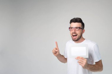 Genç adam arka planda izole edilmiş. Yüksek sesle konuş ve parmağınla işaret et. Elinde boş beyaz bir kağıt parçası tut. Gözlük tak. Stüdyoda yalnız.