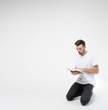 Genç adam arka planda izole edilmiş. Dizlerinin üstüne çök ve kitap oku. Odada tek başına tut. Akıllı adam çalışıyor ya da öğreniyor..