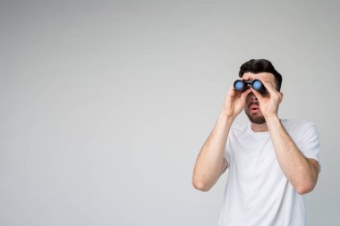 Genç adam arka planda izole edilmiş. Adam bir dürbüne çok uzak görünüyor. Stüdyoda tek başına dur. Resimdeki sıradan görünüşlü adam. Soruşturma.