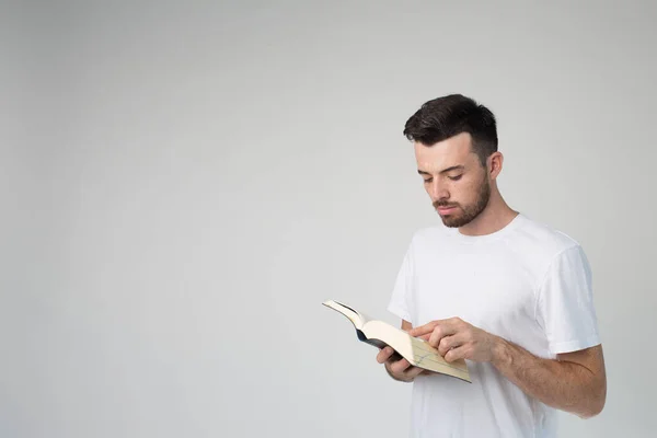 Young man isolated over background. Side view of guy reading book and standing in room alone. Point with finger. Smart wise young man on picture. — Stock Photo, Image