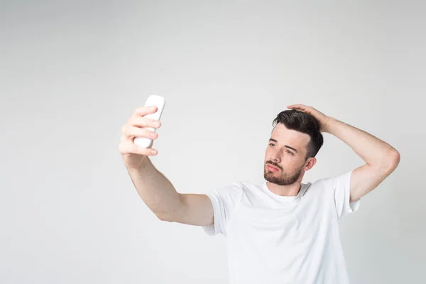 Young man isolated over background. Guy posing for selfie. Using smartphone for taking pictures. Alone in room. Male model hold hand on head. — Stock Photo, Image