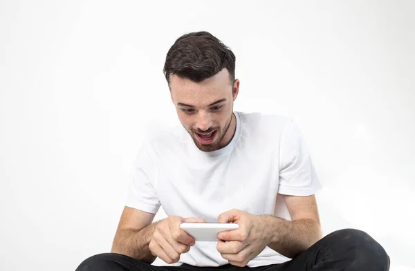 Young man isolated over background. Guy sit alone and play games on smartphone or using it with both hands. Modern technologies. Concentrated and hardplaying person. — Stock Photo, Image